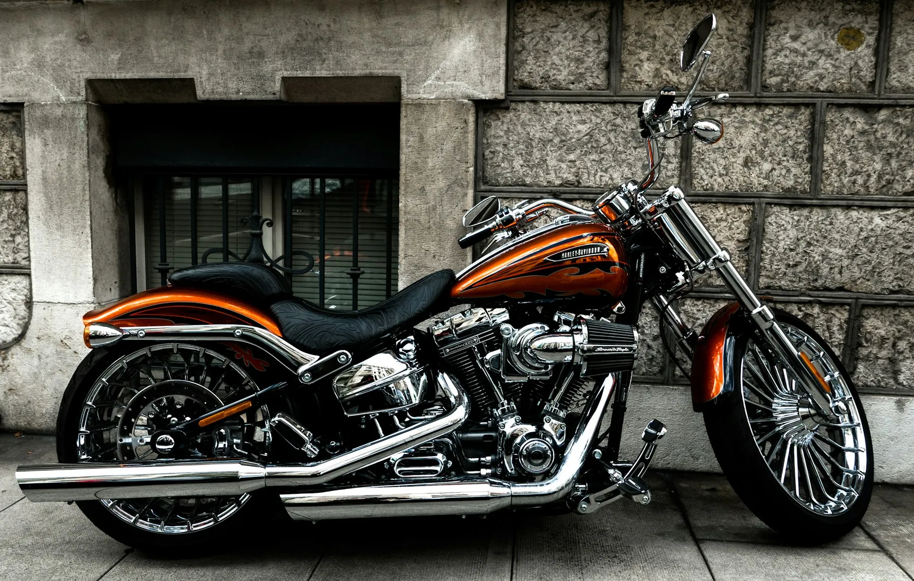 Moto custom naranja aparcada junto a un muro de piedra